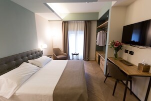 Camera d'albergo con un letto grande, una scrivania, una sedia, una TV, un armadio e una finestra con tende.