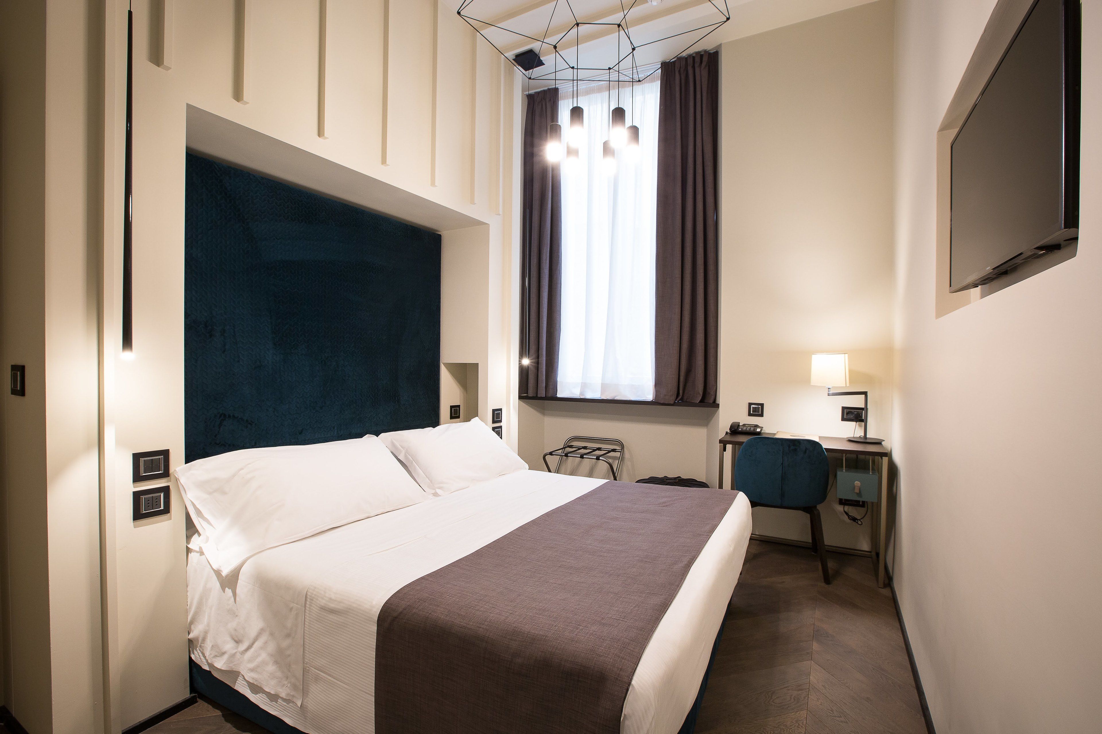 A hotel room with a bed, a desk, a chair, a TV, and a window with curtains.