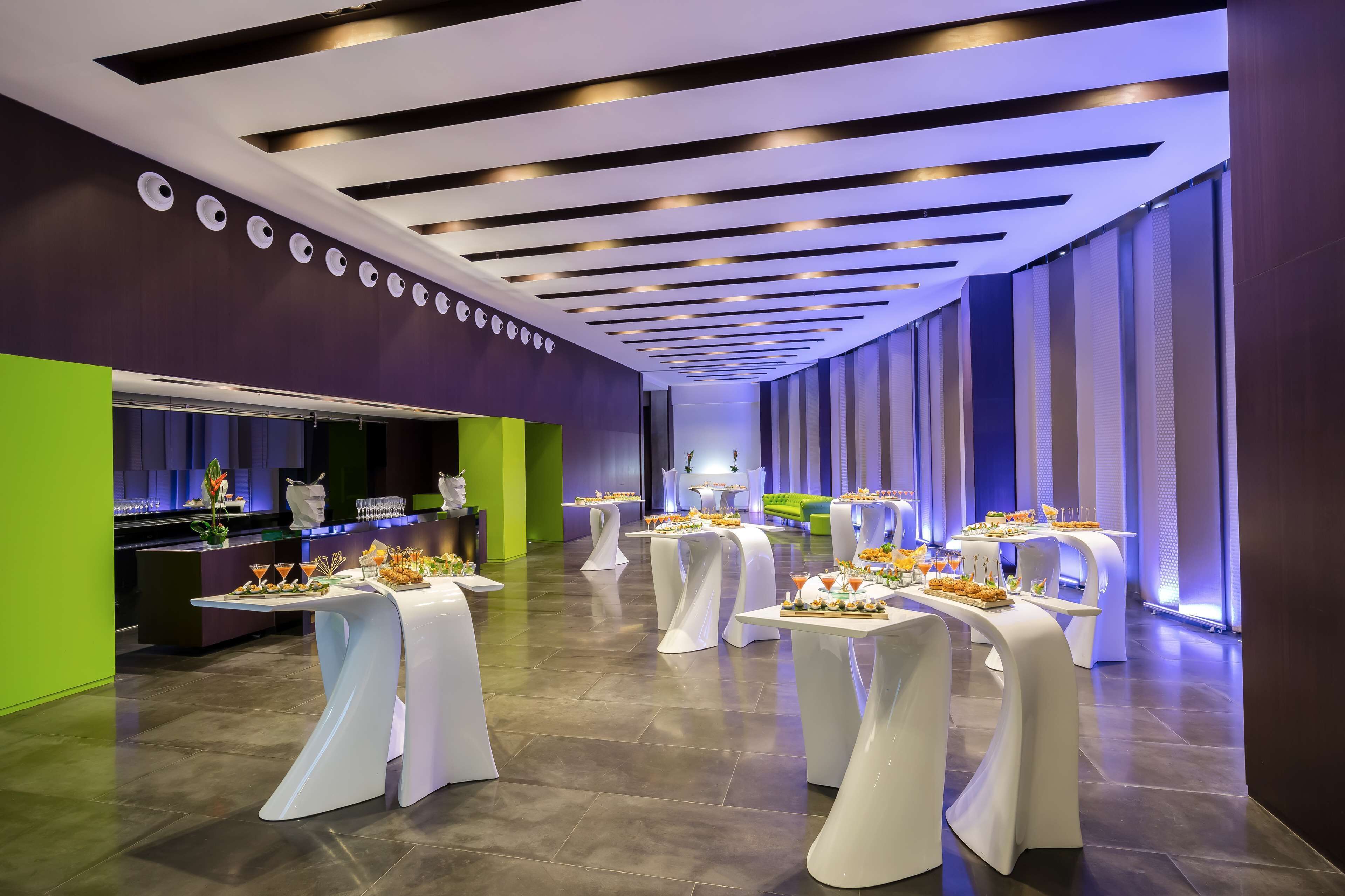 Un moderno vestíbulo de hotel con un mostrador de recepción alargado, varias mesas con manteles blancos y una pared de acento verde brillante.
