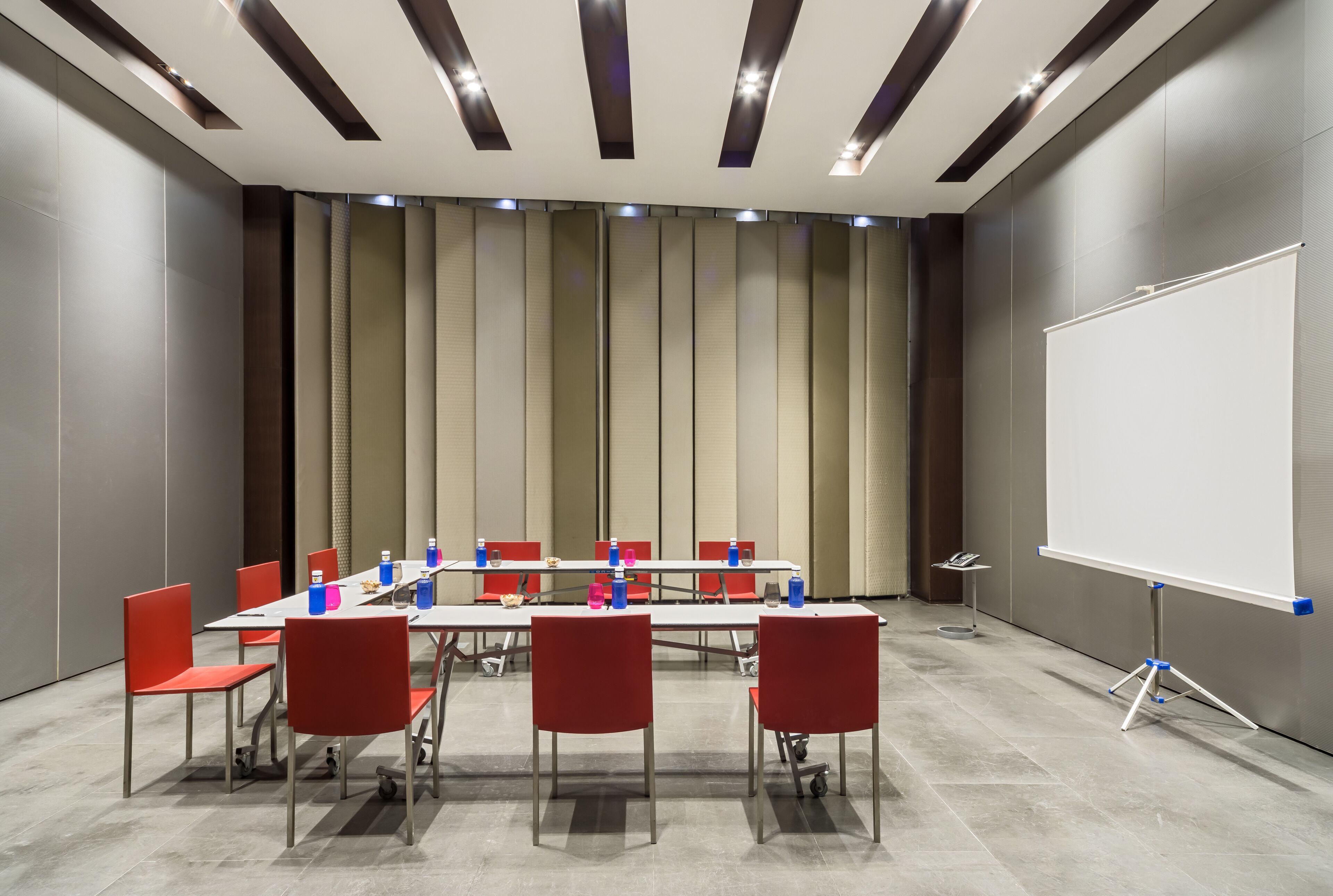 Ein Konferenzraum mit einer Wandtafel, roten Stühlen und einem langen Tisch.