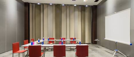 A conference room with a whiteboard, red chairs, and a long table.