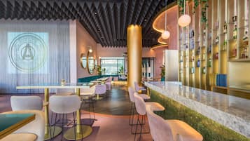 Un espace bar moderne avec un comptoir incurvé, des tables et des chaises rondes, et un mur entièrement recouvert de bouteilles d’alcool.