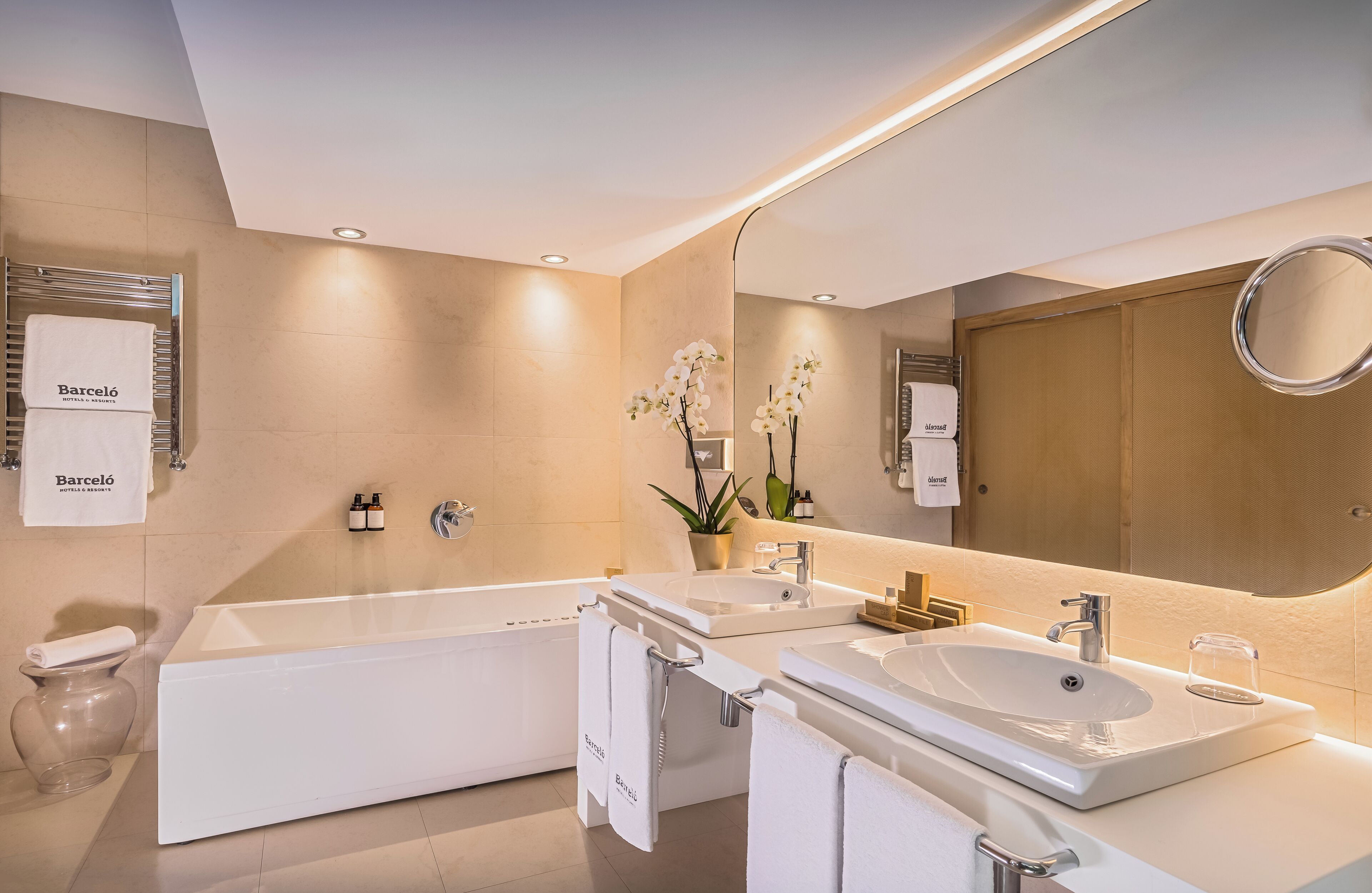 A modern bathroom with a bathtub, two sinks, a large mirror, and a toilet.