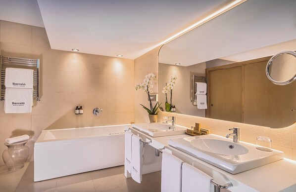 Un baño moderno con bañera, dos lavamanos, un espejo grande y un inodoro.