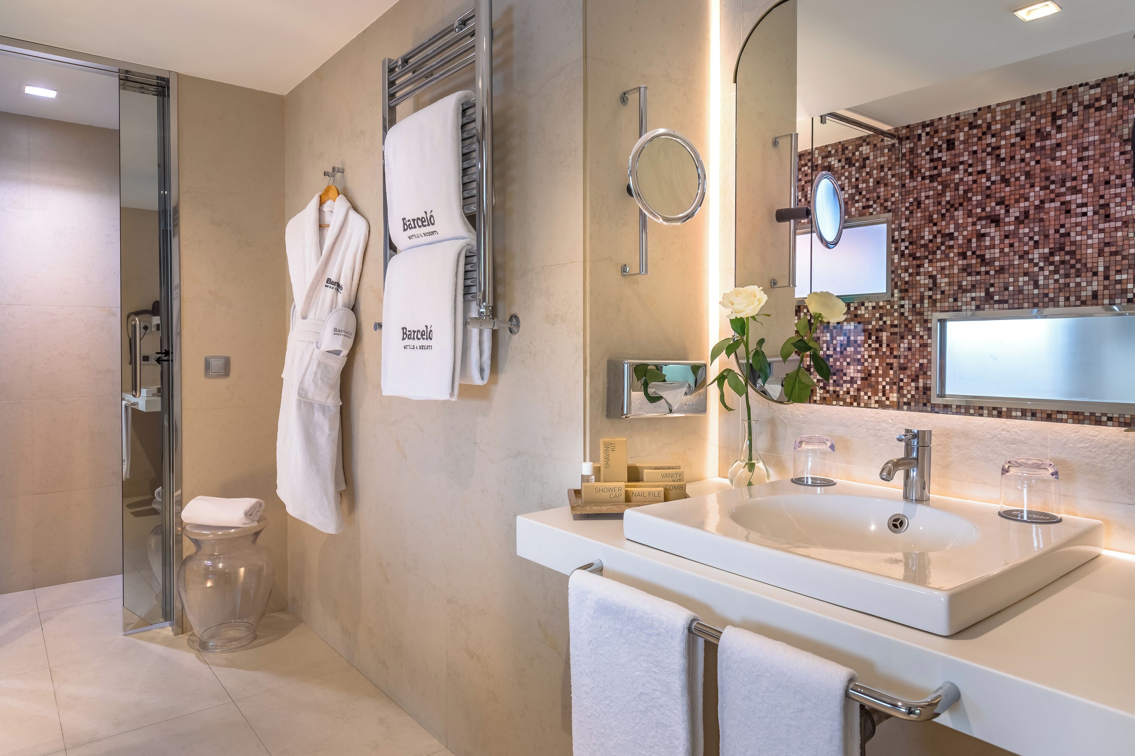 Un baño moderno con cabina de ducha de vidrio, un lavabo blanco con espejo y una pared de mosaicos.