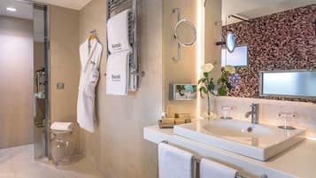 Un baño moderno con cabina de ducha de vidrio, un lavabo blanco con espejo y una pared de mosaicos.