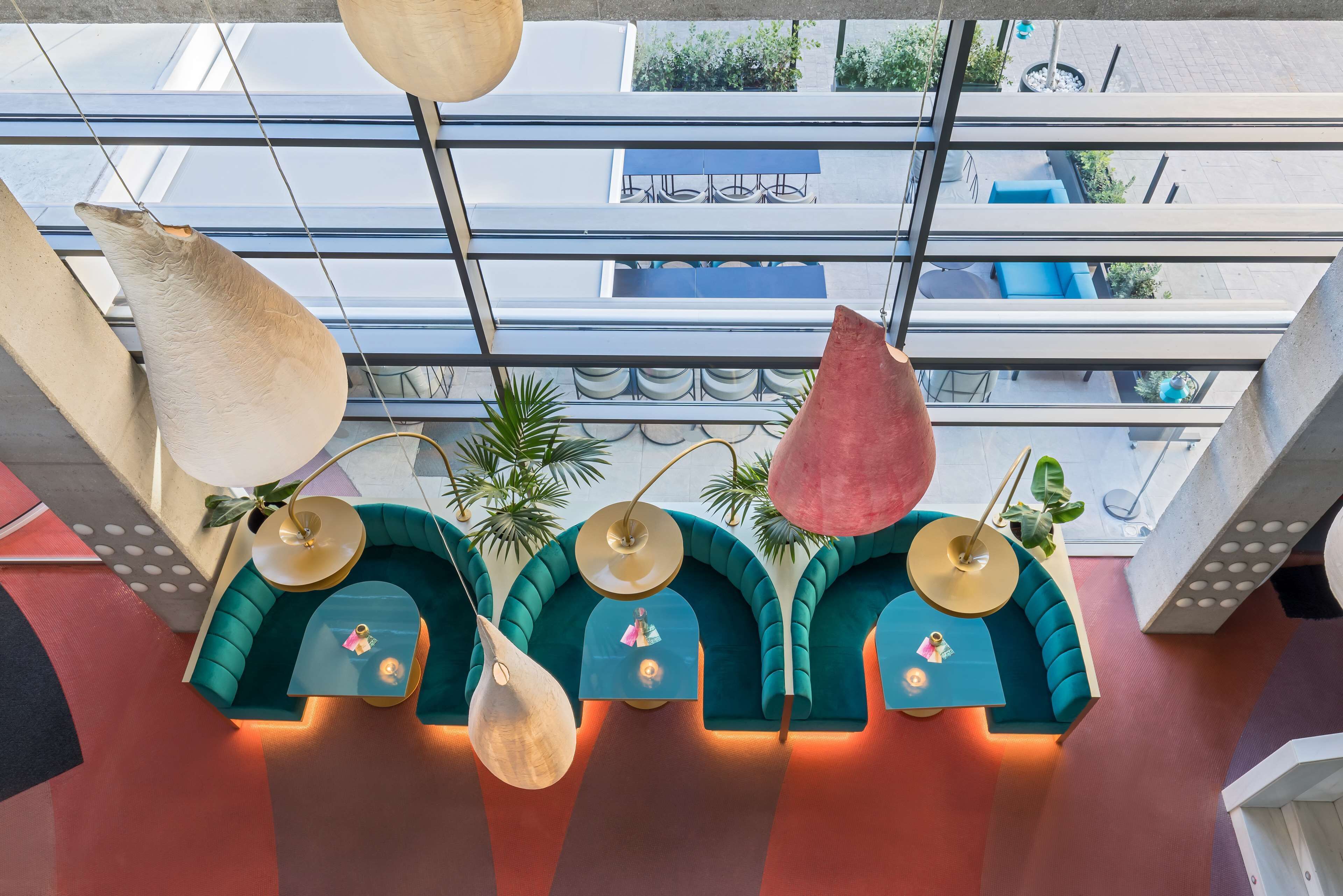 Un interior moderno con sofás color turquesa y mesas redondas, una lámpara colgante y vistas al exterior a través de amplios ventanales.
