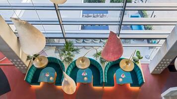 Un interior moderno con sofás color turquesa y mesas redondas, una lámpara colgante y vistas al exterior a través de amplios ventanales.