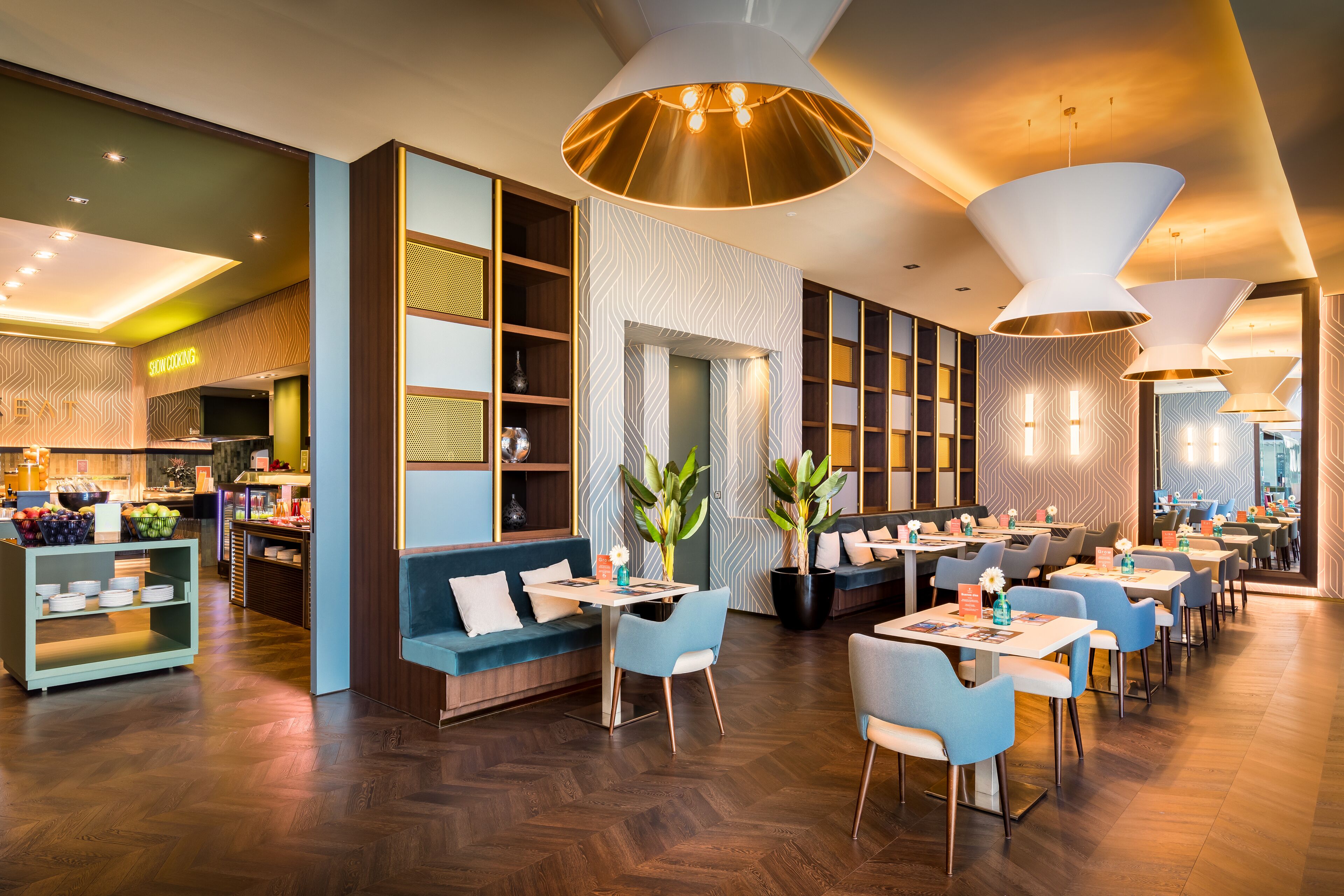 A modern restaurant with a herringbone wood floor, blue and grey seating, and pendant lighting.