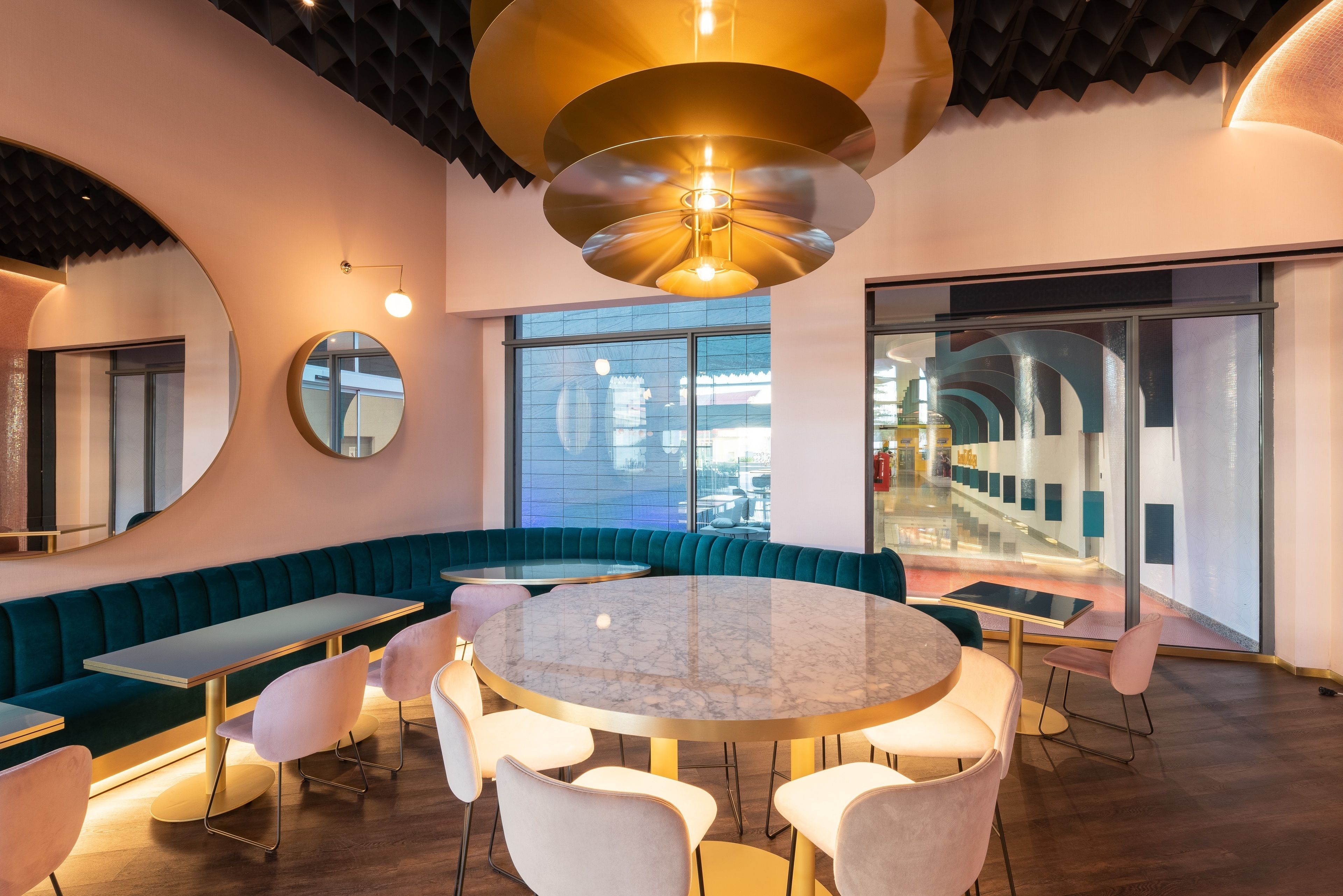 Un interior moderno con una mesa redonda de mármol rodeada de sillas blancas, asientos color turquesa y un espejo grande.