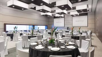 A conference room with round tables, white chairs, and black tablecloths.