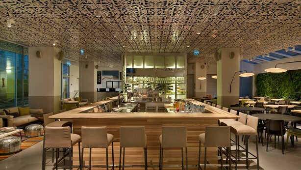 A modern bar area with a central bar counter, seating, and a unique ceiling design.