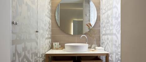 A modern bathroom with a round mirror, a white sink, and a shelf with folded towels.