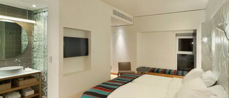 A modern hotel room with a large bed, a bedside table, a flat-screen TV, a bathroom with a sink and mirror, and a window.