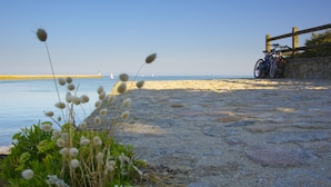 A coastal walkway with a bicycle parked by a stone wall, leading to a sandy beach.