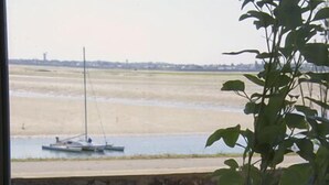 A table with a dessert, a glass of red wine, and a view of a beach with a sailboat.