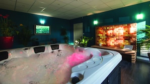 A spa room with a hot tub, seating area, and decorative wall.