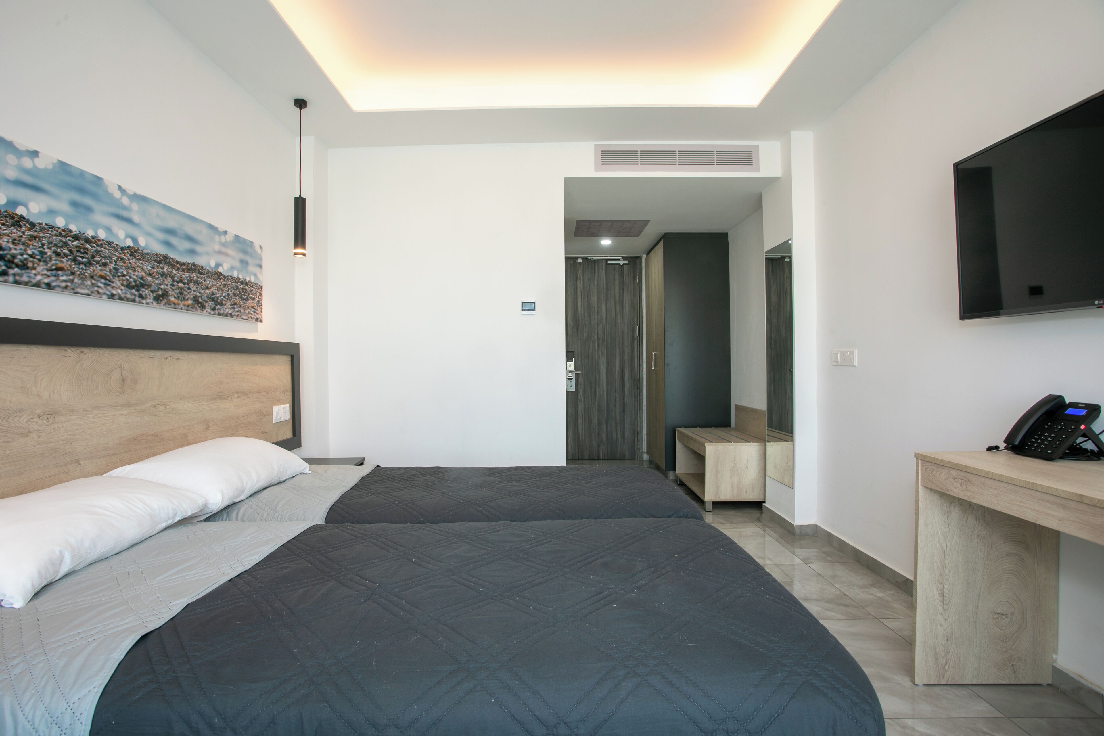 A modern hotel room with two beds, a desk, a flat-screen TV, and a painting on the wall.