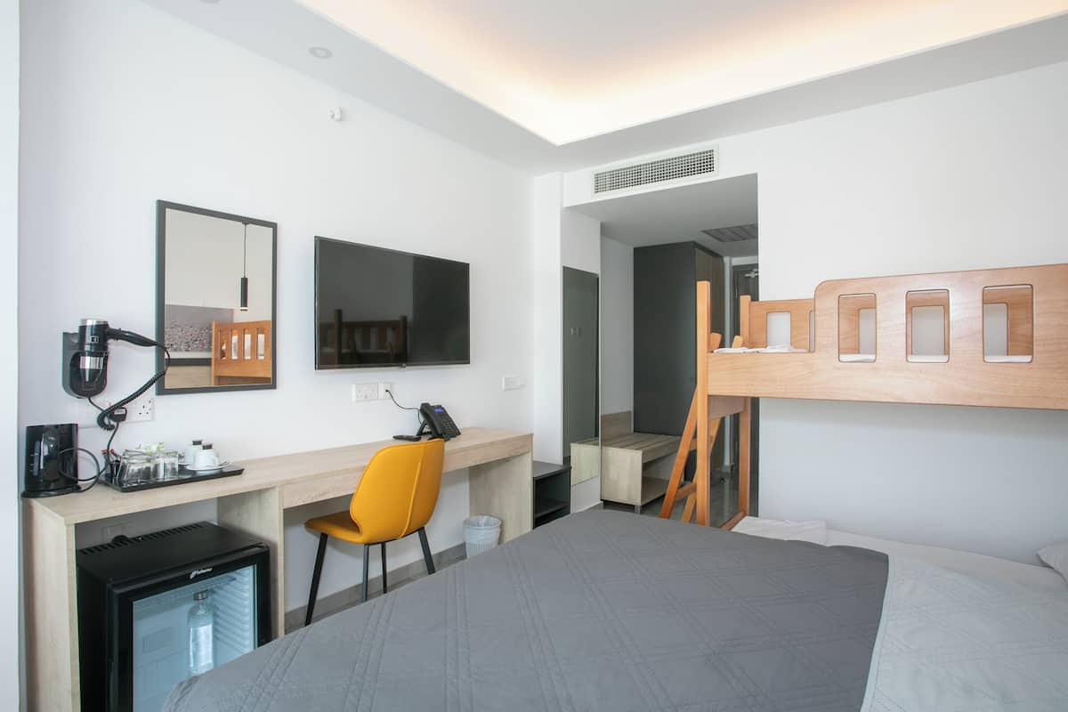 Quarto de hotel moderno com cama, escrivaninha, cadeira e um pequeno frigorífico.