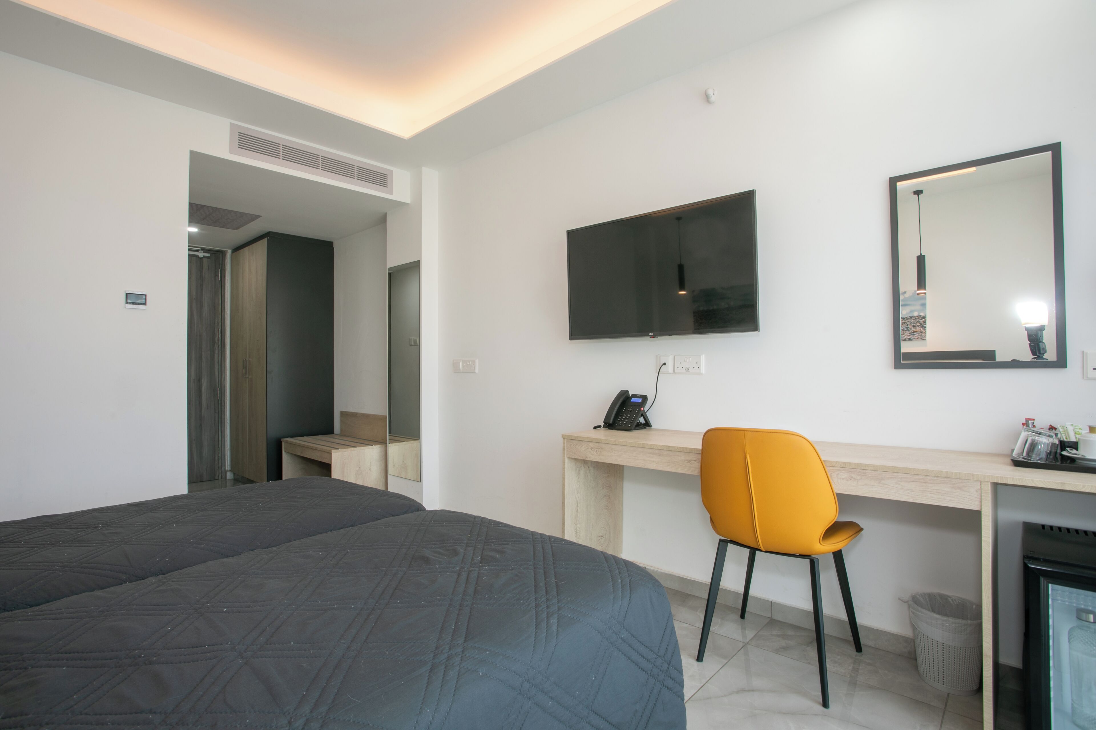 A hotel room with a bed, a desk with a chair, a television, and a mirror.