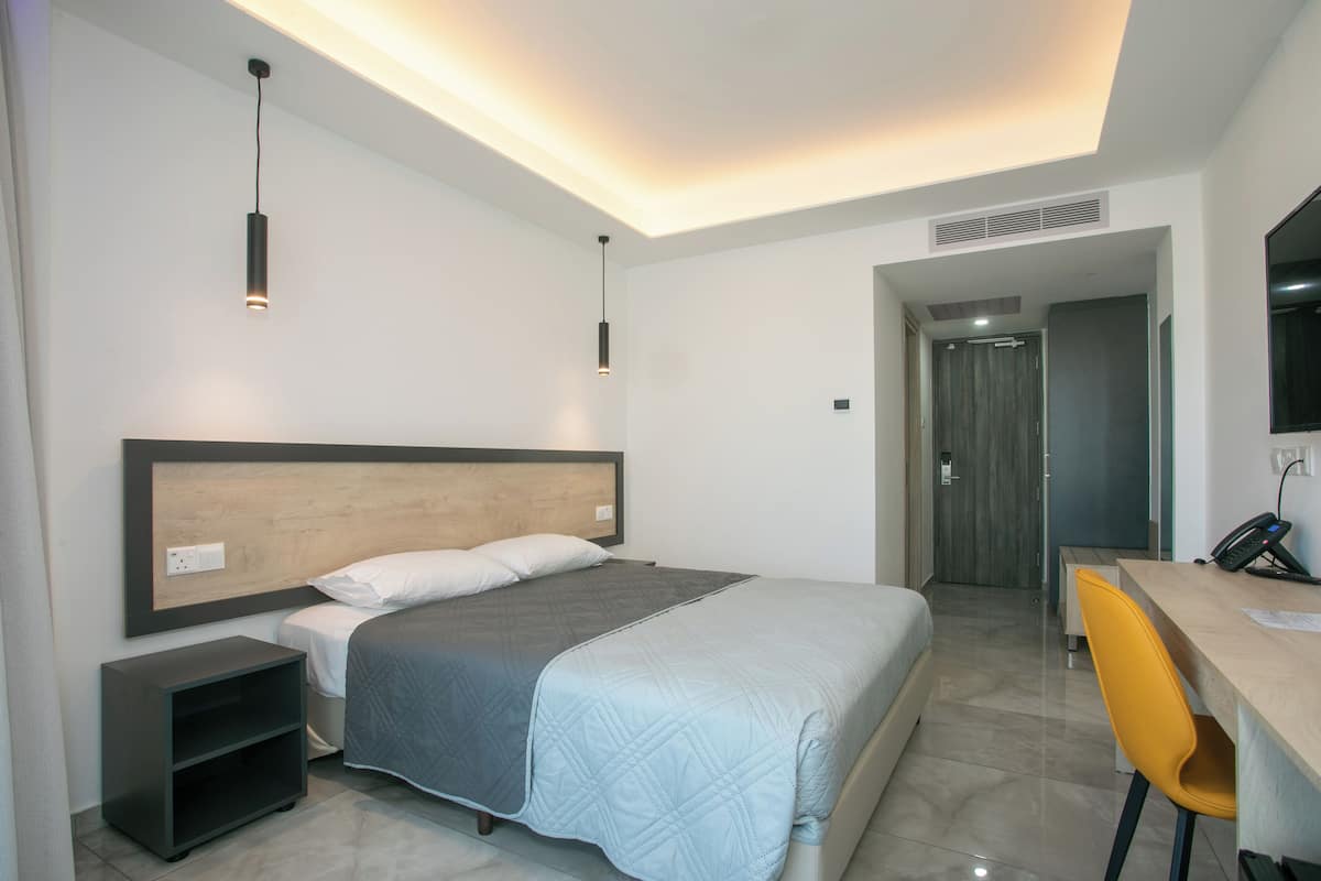 Quarto de hotel moderno com cama, mesa de cabeceira, escrivaninha e cadeira.