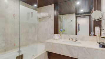 Un baño moderno con ducha de vidrio, lavamanos de mármol y un espejo grande.