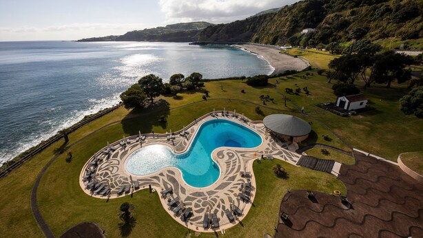 A resort with a large swimming pool, a beach, and a mountainous backdrop. - Pestana Bahia Praia Nature & Beach Resort (Vila Franca do Campo)