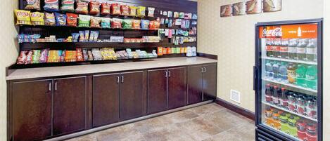 A snack display with various chips and snacks, a beverage refrigerator with multiple drink options, and a tiled floor.