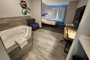 A hotel room with a large bathtub, a bed, a desk with a chair, and a television. - La Quinta Inn & Suites by Wyndham Warner Robins - Robins AFB (Warner Robins)