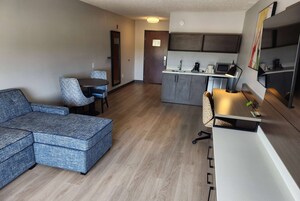 A modern living room with a sectional sofa, a dining table with chairs, a kitchen area with a microwave and coffee maker, and a large mirror on the wall.