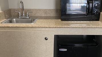 Una kitchenette compacta con un lavaplatos de acero inoxidable, un microondas negro y un lavavajillas negro.