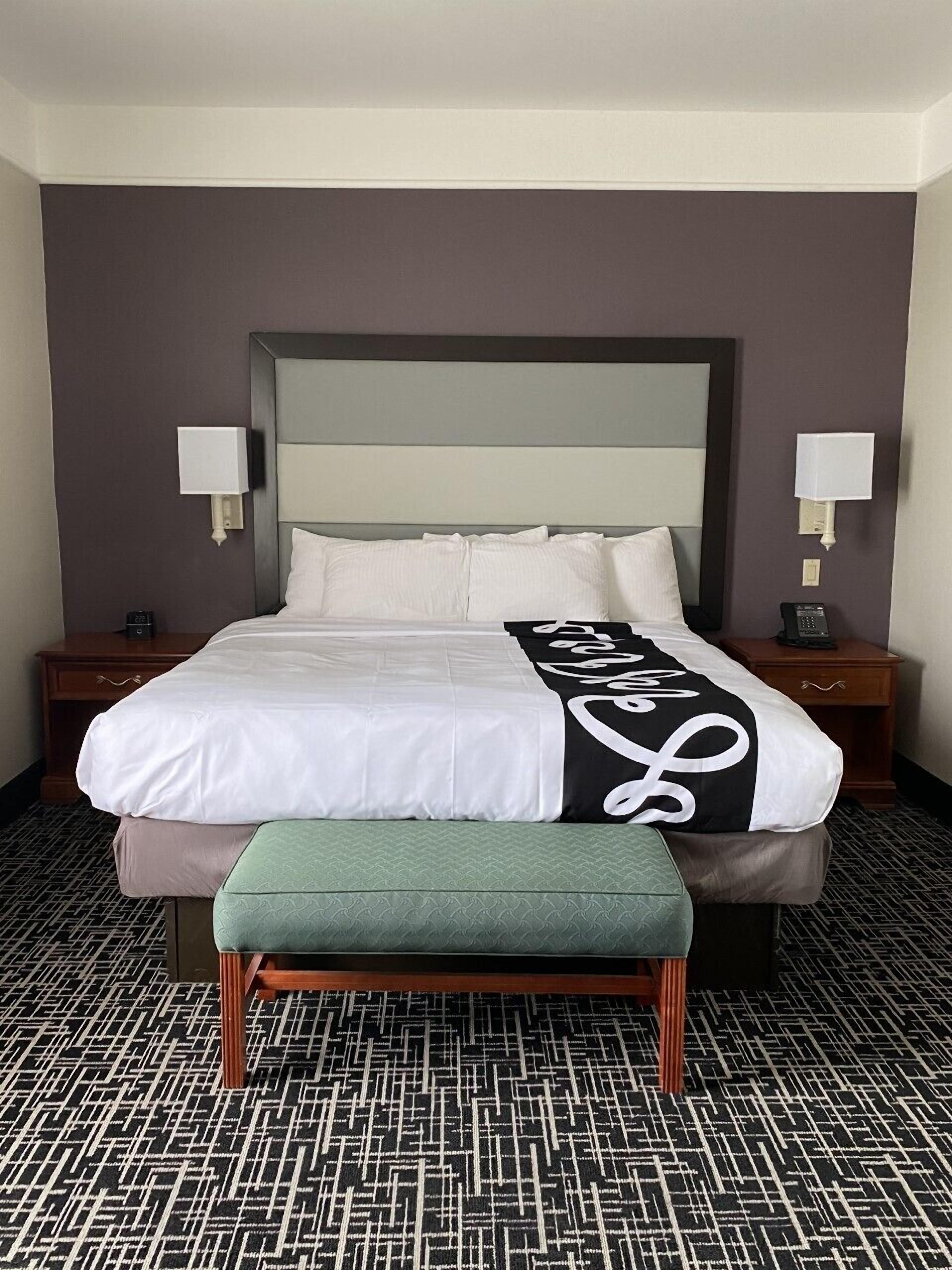 A hotel room with a large bed, two bedside tables, a bench, and patterned carpet.