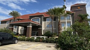 A La Quinta hotel with a red roof, multiple floors, and a parking lot. - Quality Inn and Suites (Rosenberg)