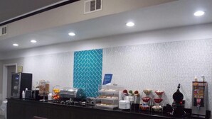 A hotel breakfast area with a buffet counter, microwave, and seating area. - Quality Inn and Suites (Rosenberg)