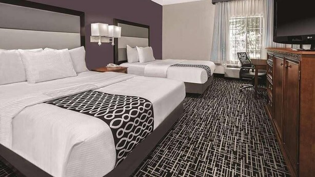 A hotel room with two beds, a TV, a desk, and a patterned carpet. - Quality Inn and Suites (Rosenberg)