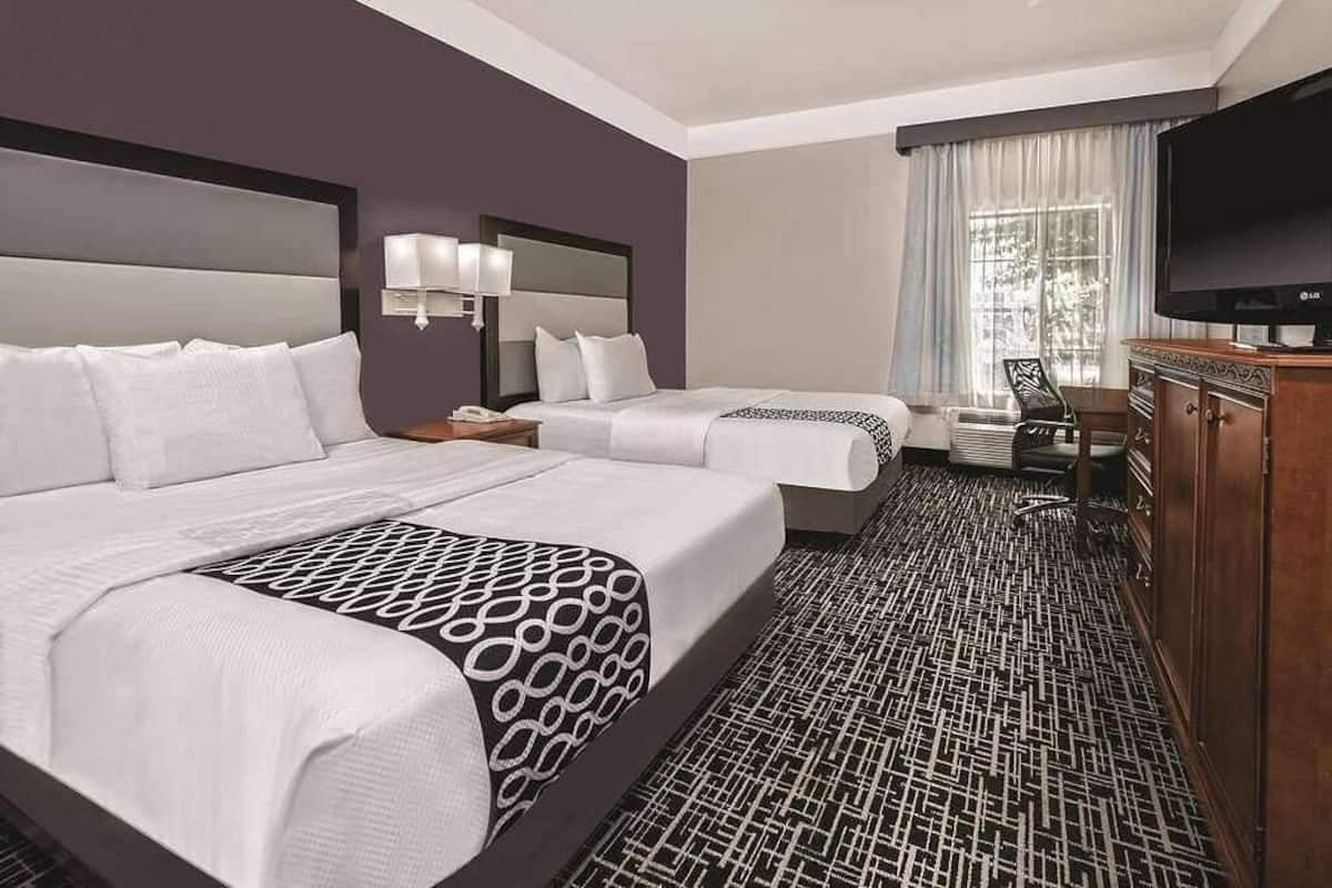 A hotel room with two beds, a TV, a desk, and a patterned carpet.