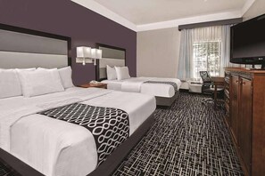 A hotel room with two beds, a TV, a desk, and a patterned carpet.