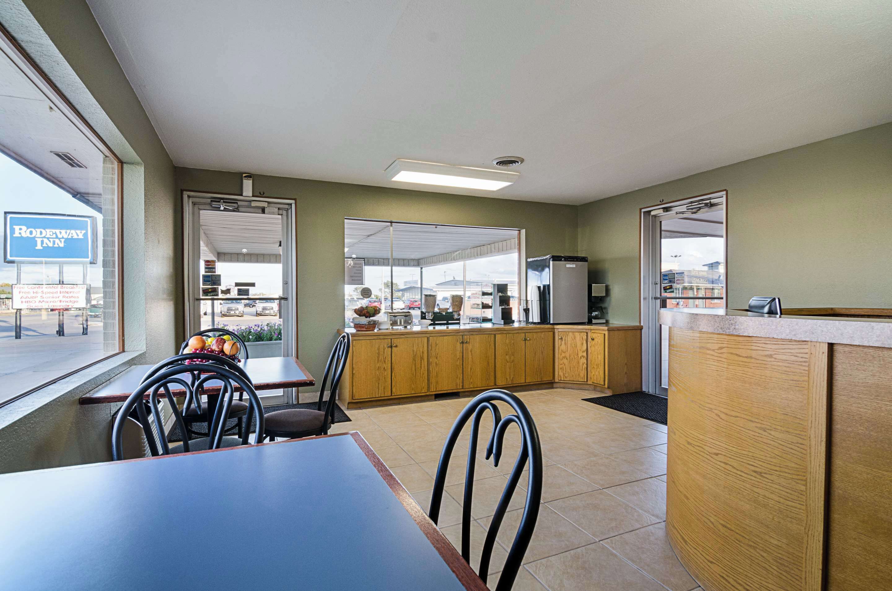 A hotel kitchen with wooden cabinets, a refrigerator, and a window with a sign for Rodeway Inn.