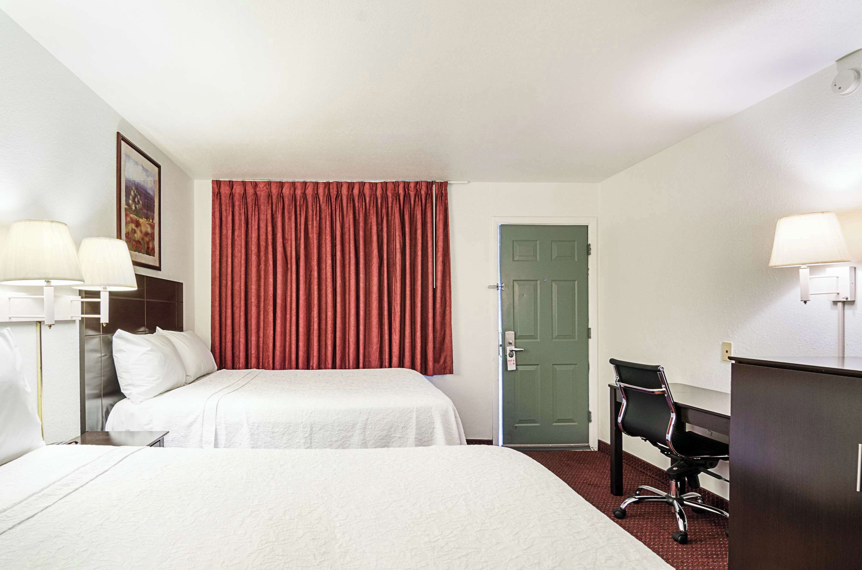 Habitación de hotel con dos camas, un escritorio, una silla y una puerta verde.