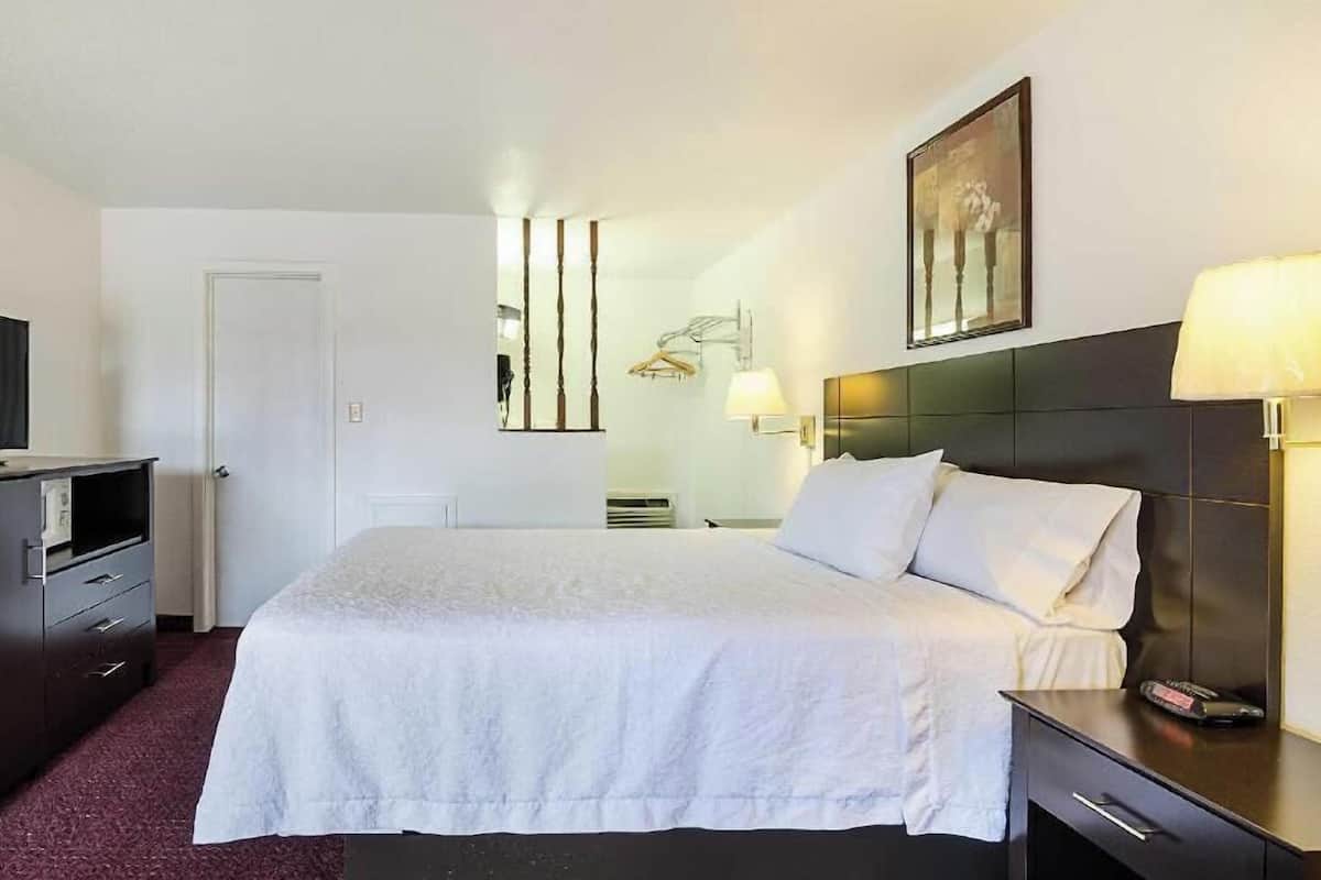 Quarto de hotel com cama, mesa de cabeceira, luminária e televisão.