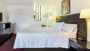 A hotel room with a large bed, a bedside table with a lamp, a dresser, and a television.