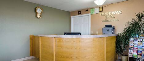 Un mostrador de recepción con detalles de madera, un reloj en la pared y un letrero de bienvenida para Rodeway Inn.
