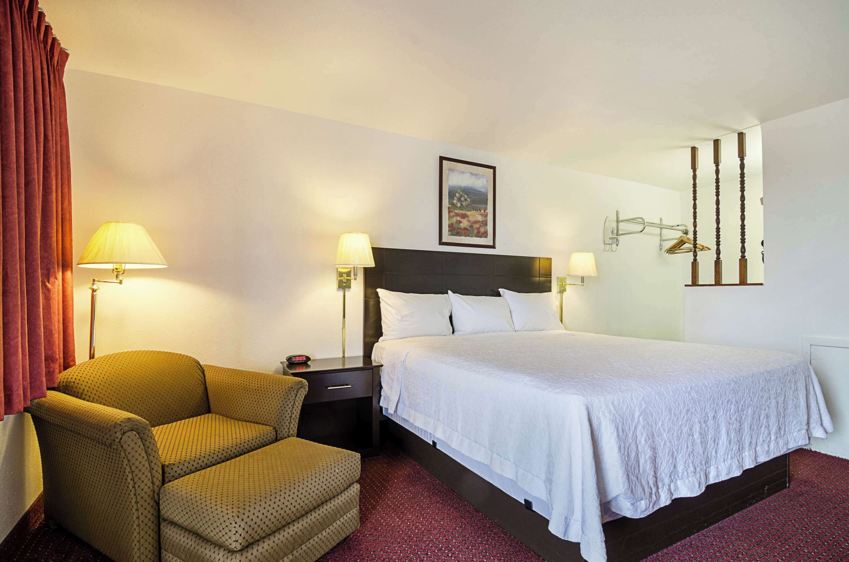 Una camera d'albergo con un letto, una sedia, un comodino e una lampada.