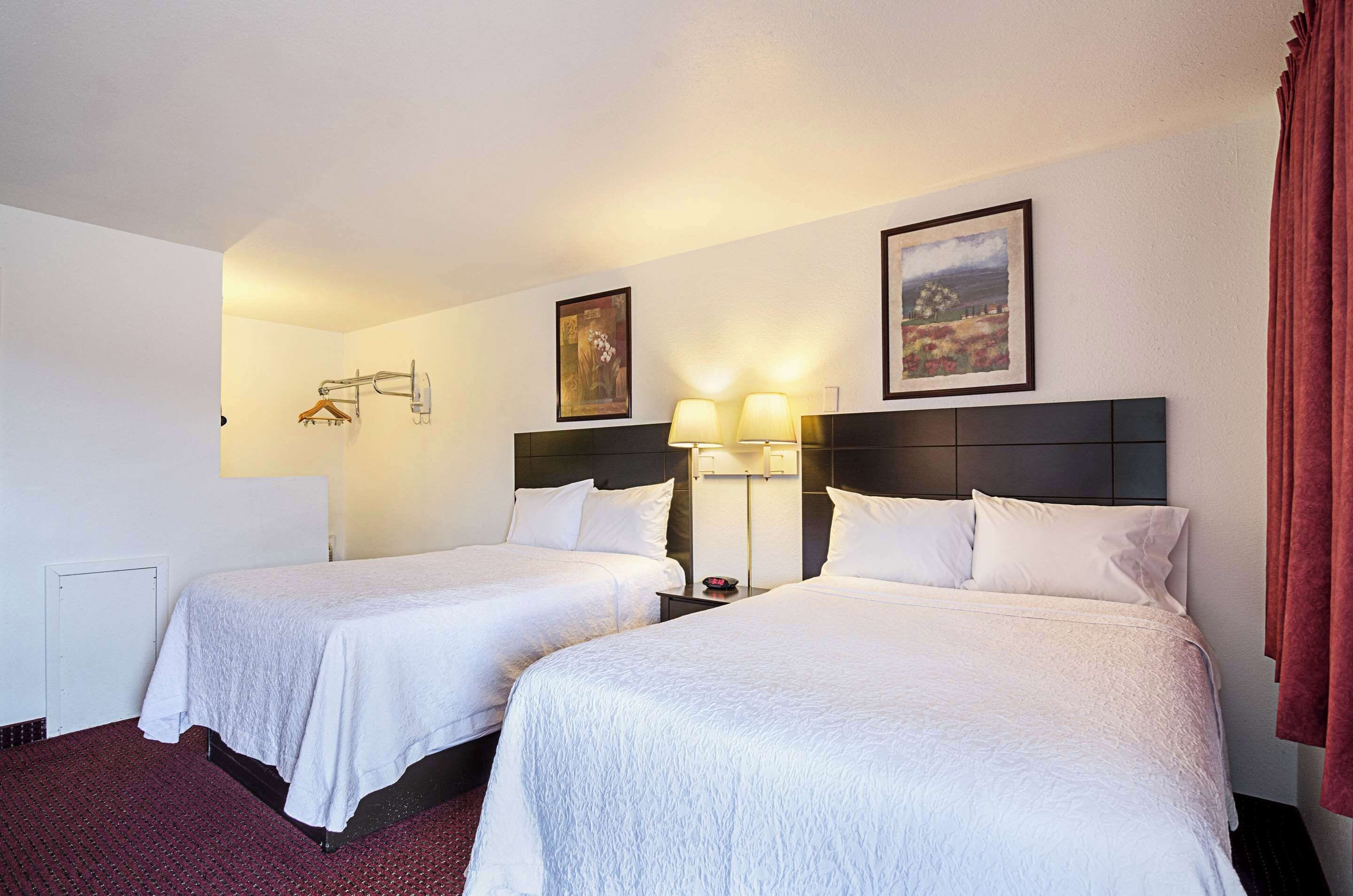 Habitación de hotel con dos camas, una mesita de noche, una lámpara y un cuadro en la pared.