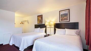 Habitación de hotel con dos camas, una mesita de noche, una lámpara y un cuadro en la pared.