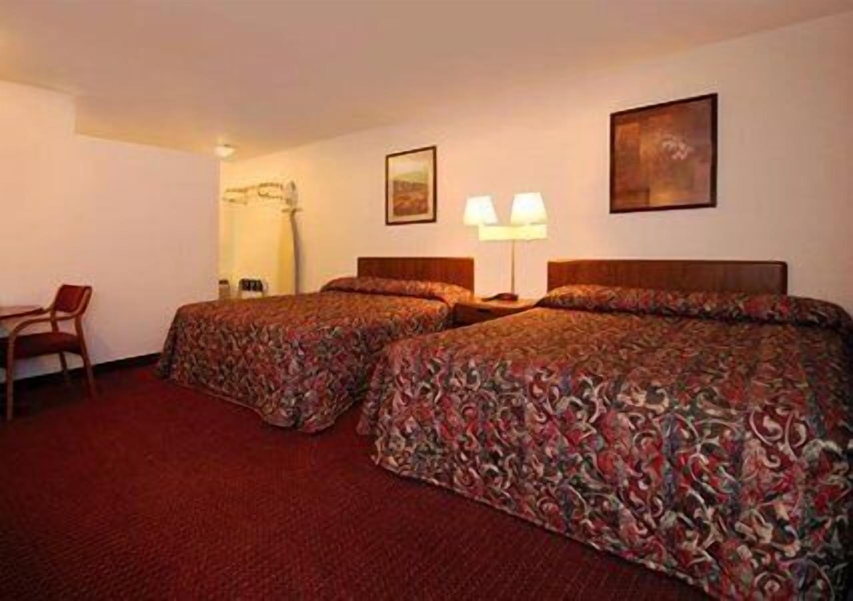 A hotel room with two beds, a desk, and a chair.