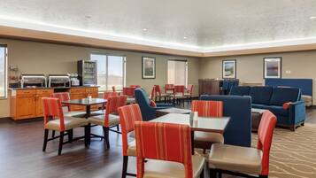 A hotel lobby with a dining area, seating arrangements, and a kitchenette.