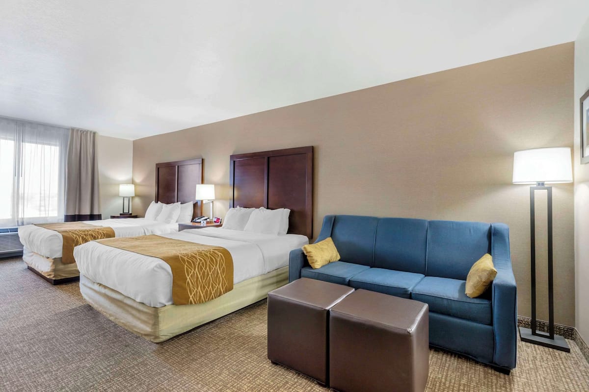 Ein Hotelzimmer mit zwei Betten, einem blauen Sofa, einem kleinen Tisch und einer Stehlampe.