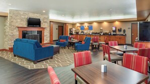 Un vestíbulo de hotel con pared de piedra, un televisor de pantalla plana, una chimenea, asientos azules y rojos, una barra de café y una gran pantalla de televisión.