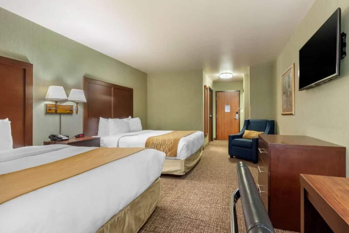 Ein Hotelzimmer mit zwei Betten, einem Schreibtisch, einem Stuhl, einem Fernseher und einer Lampe.